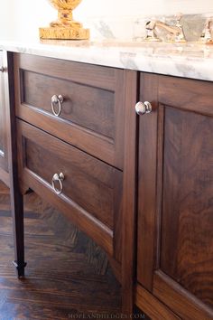 a bathroom vanity with marble top and wooden cabinetry on the bottom, next to a gold urn