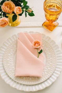 a white plate topped with pink napkins next to a glass vase filled with flowers