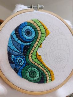 a colorful hand embroidered art piece on a white cloth with a wooden hoop hanging from it