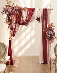 a wedding arch decorated with red and white draping, flowers and greenery