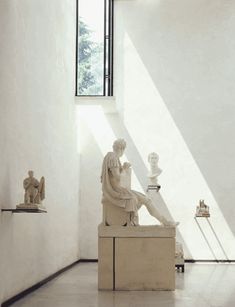 a room filled with statues and windows next to each other in white walls, on either side of the wall is a window