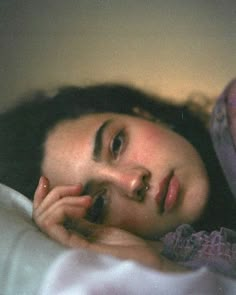 a woman laying on top of a bed next to a pink pillow and blanket with her hand near her face