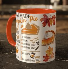 an orange and white coffee mug sitting on top of a counter next to a maple leaf