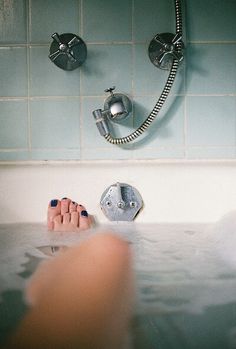 a woman's feet in the bathtub with water running down it and a faucet above her head