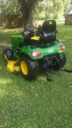 a green lawn mower sitting on top of a lush green field next to a tree