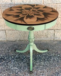 a green table with a flower painted on it's top sitting in front of a brick wall