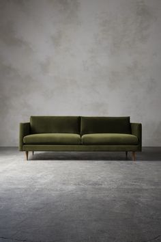 a green couch sitting on top of a cement floor in front of a gray wall