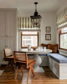 a kitchen with a table, bench and window seat in front of two windows that have roman shades on them