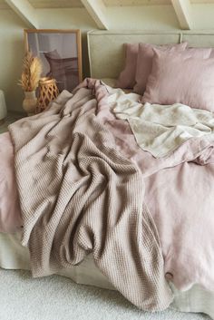 an unmade bed with pink sheets and blankets on top of it, in a bedroom