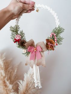 a hand holding a christmas wreath with pine cones and candy canes