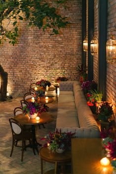 an outdoor seating area with lit candles and potted plants on the side of it