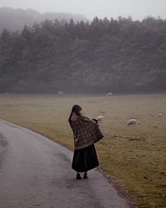 a woman walking down a road with sheep in the background