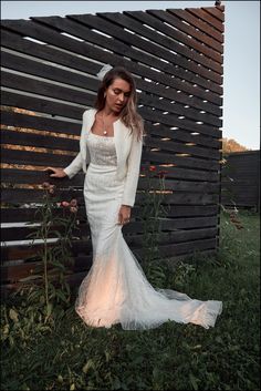 a woman in a white wedding dress leaning against a wooden wall with flowers on it