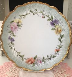 a plate with flowers painted on it sitting on a doily