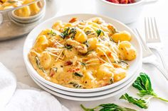 a white plate topped with pasta covered in cheese and spinach next to bowls of fruit