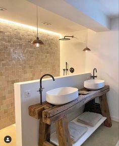 two white sinks sitting on top of a wooden table next to a wall mounted faucet