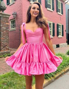 a woman standing in front of a pink house wearing a short dress with ruffles