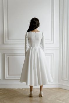 a woman in a white dress standing against a wall with her back to the camera