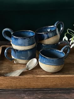 four blue and white ceramic cups with spoons on a wooden tray next to flowers