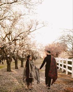 two people holding hands and walking through an orchard with trees in the backgroud