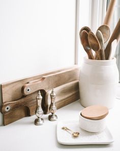 utensils and spoons are sitting in a white container on a counter next to a window