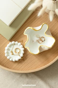 two pieces of jewelry sitting on top of a wooden table next to a vase with flowers