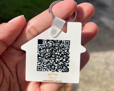 a hand holding a house shaped keychain with a qr code on it