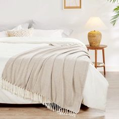 a bed with white sheets and blankets on top of it next to a table lamp