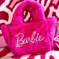 a pink purse with the word barbie on it sitting on a red and white blanket