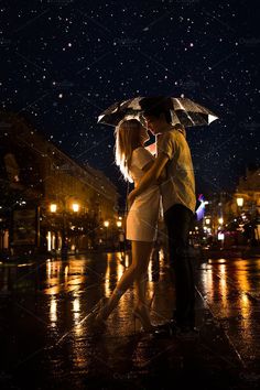 a man and woman standing under an umbrella in the rain on a city street at night