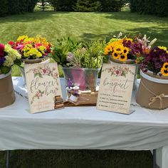 three buckets filled with flowers sitting on top of a white tablecloth covered field