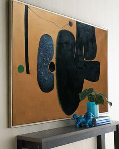 an abstract painting hangs on the wall above a table with a blue vase and books