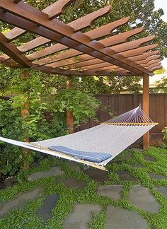 a hammock hanging from a pergolated roof in a backyard with green grass