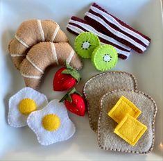 an assortment of felt food on a plate with eggs, strawberries, and toast