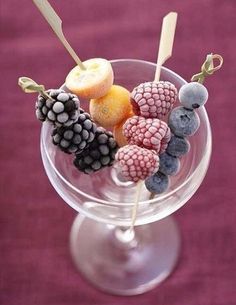 a glass filled with fruit on top of a purple table next to a pink wall