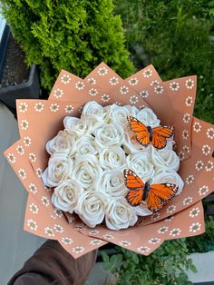 a bouquet of white roses with two butterflies on them in a pink paper wrapper