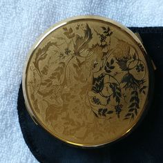 a gold colored compact case sitting on top of a blue cloth