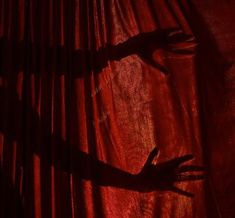 the shadow of a woman's arm on a red curtain with her hands in the air