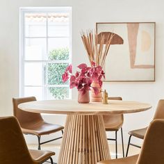 a dining room table with chairs and flowers in vases on the top, next to a window