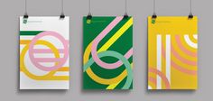 three posters hanging from strings on a gray wall, each with different colors and shapes