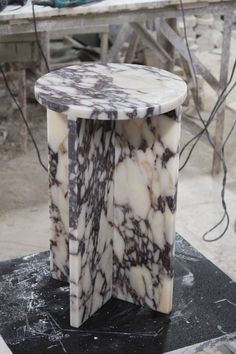 a white and brown marble table sitting on top of a black piece of wood next to a building