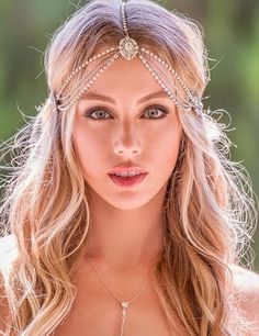 a woman with long blonde hair wearing a head piece and jewelry on her face, looking at the camera