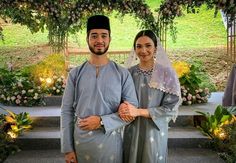 two people standing next to each other in front of flowers and greenery on the ground