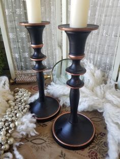 two black candlesticks sitting on top of a rug next to a window with white curtains