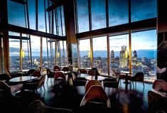 an empty restaurant with large windows overlooking the city at night and lit up by bright lights