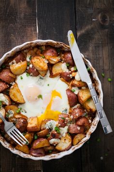 a plate with potatoes and an egg on top, next to a knife and fork