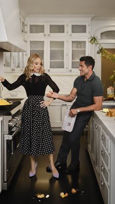 a man standing next to a woman in a black and white polka dot dress while she holds out her hand