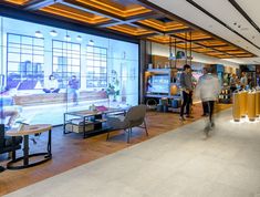 people are walking around in the lobby of an office building with large windows and wooden flooring