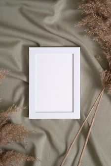 a white frame sitting on top of a bed covered in dry grass next to dried plants