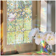 white flowers in a vase sitting on a table next to a window with sun shining through it